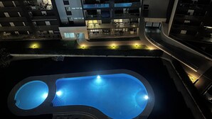 Una piscina de diseño moderno, rodeada por un edificio con múltiples balcones e iluminación exterior.