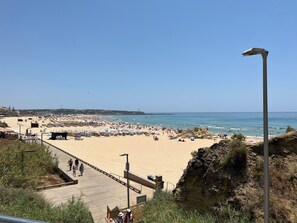 A beach with a wooden boardwalk, umbrellas, and a lighthouse in the distance. - APARTMENT 105m Praia Da Rocha 200m from the beach   (portimao)