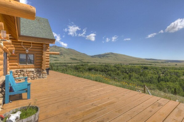 A log cabin with a wooden deck, a stone foundation, and a bench.