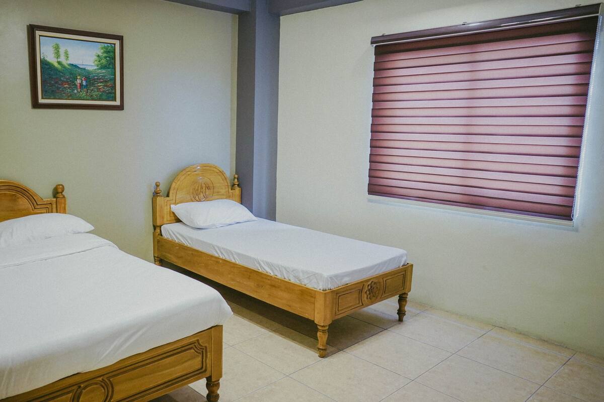 A bedroom with two wooden beds, a painting on the wall, and a window with blinds.