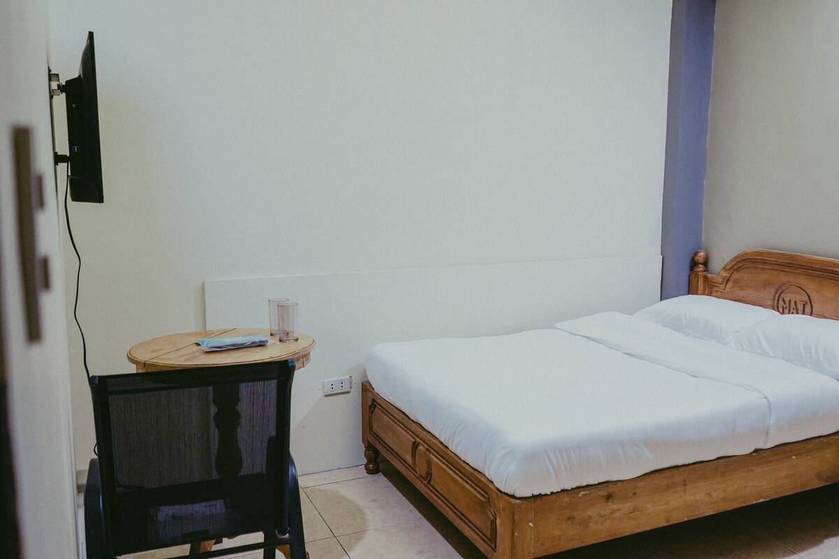 A small, simple room with a wooden bed, a small round table, and a chair.