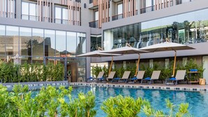 A modern hotel with a swimming pool, sun loungers, and a glass facade. - The Teak Hotel (Mae Sot)