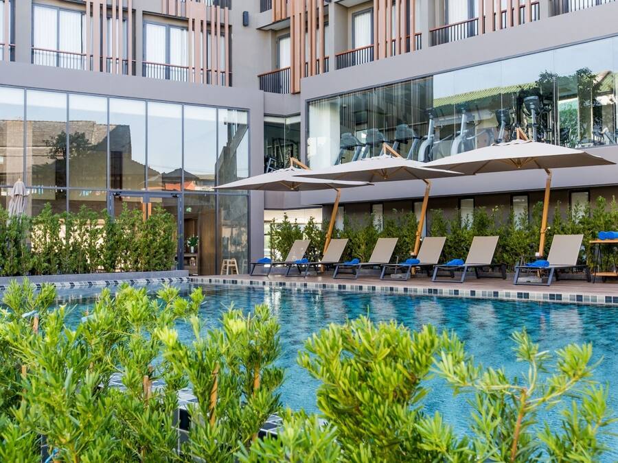 Un hotel moderno con piscina, tumbonas y fachada de vidrio.