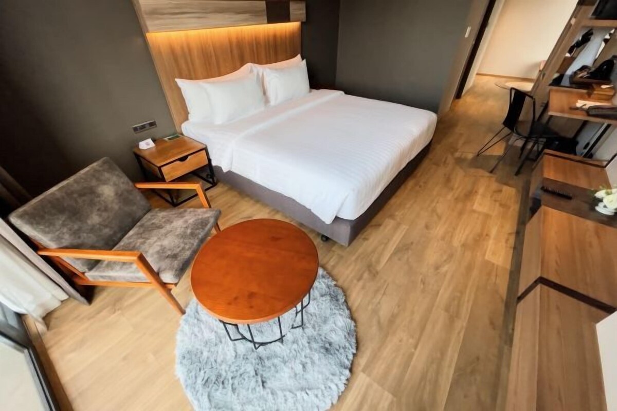 A modern hotel room with a large bed, a round wooden table, a sofa, and a small desk.