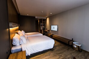 Une chambre d’hôtel moderne avec deux lits, un banc en bois, un bureau, une télévision et une poubelle.