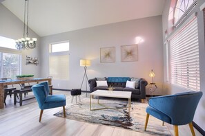 Uma sala de estar moderna com um sofá cinzento, poltronas azuis, uma mesa de centro e um candelabro.