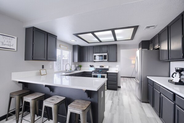Uma cozinha moderna com armários escuros, uma ilha central com banquetas, micro-ondas, fogão e geladeira.
