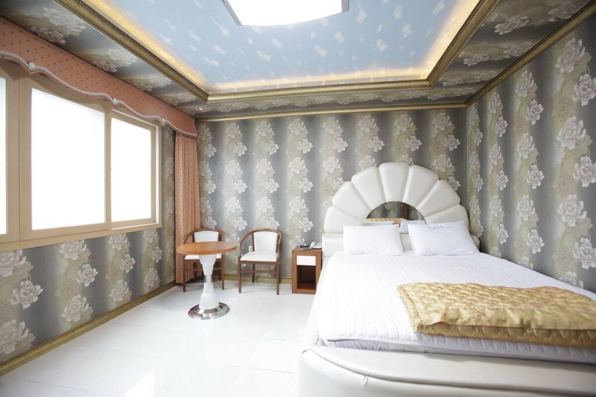 Un dormitorio con una cama grande, una mesita, dos sillas y una mesita de noche.