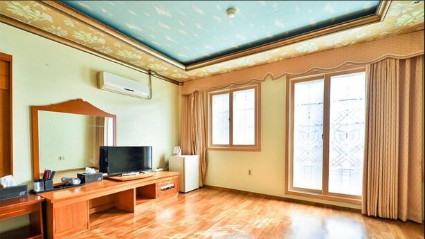 Una habitación con un escritorio de madera, televisión y un amplio ventanal con cortinas.