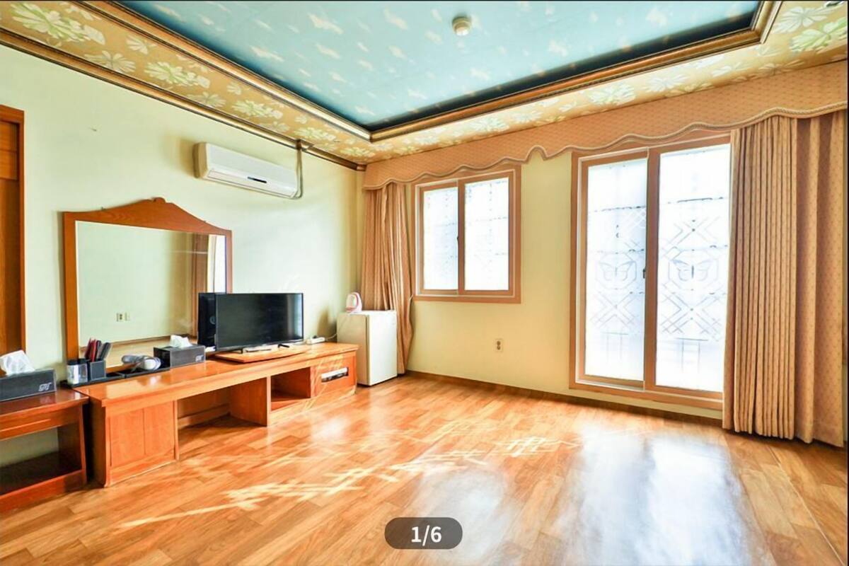 Una habitación con un escritorio de madera, televisión y un amplio ventanal con cortinas.