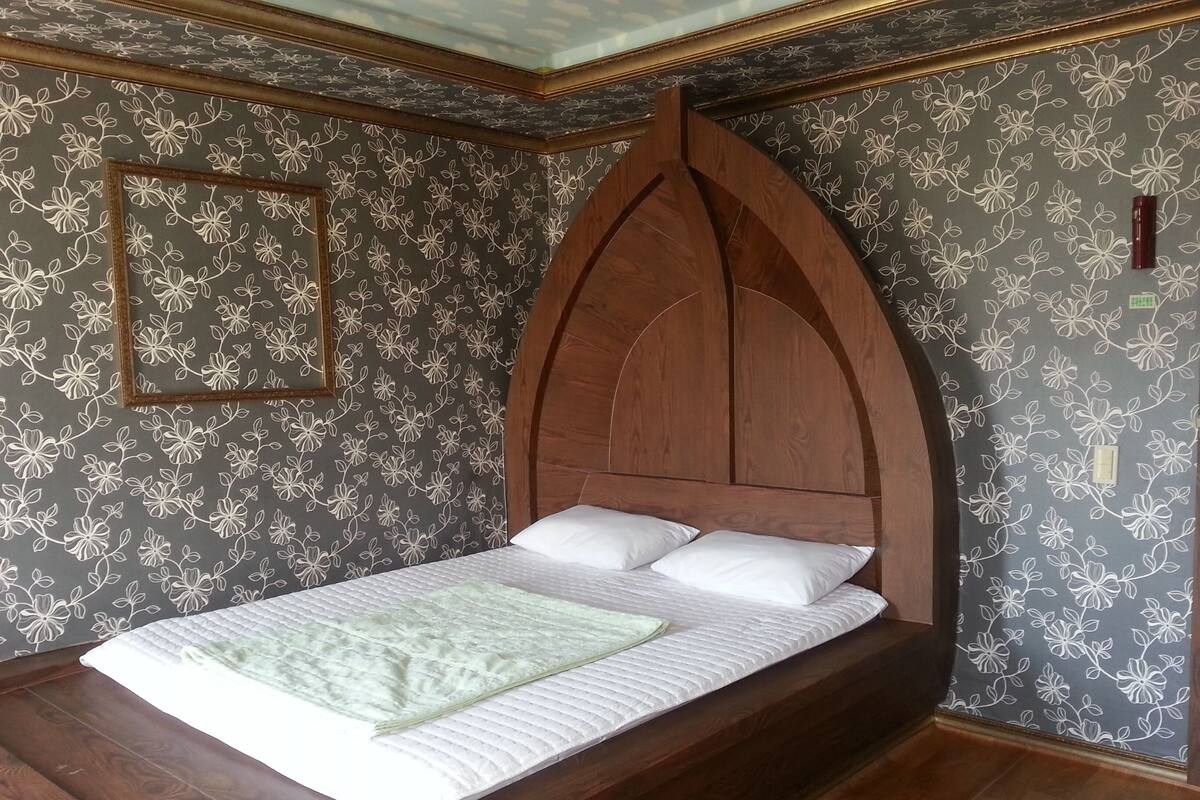 Un dormitorio con cabecera de madera con arco, cama con ropa blanca y papel tapiz estampado con flores.