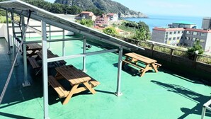 Una terraza en la azotea con mesas de picnic y estructura de techo metálico.