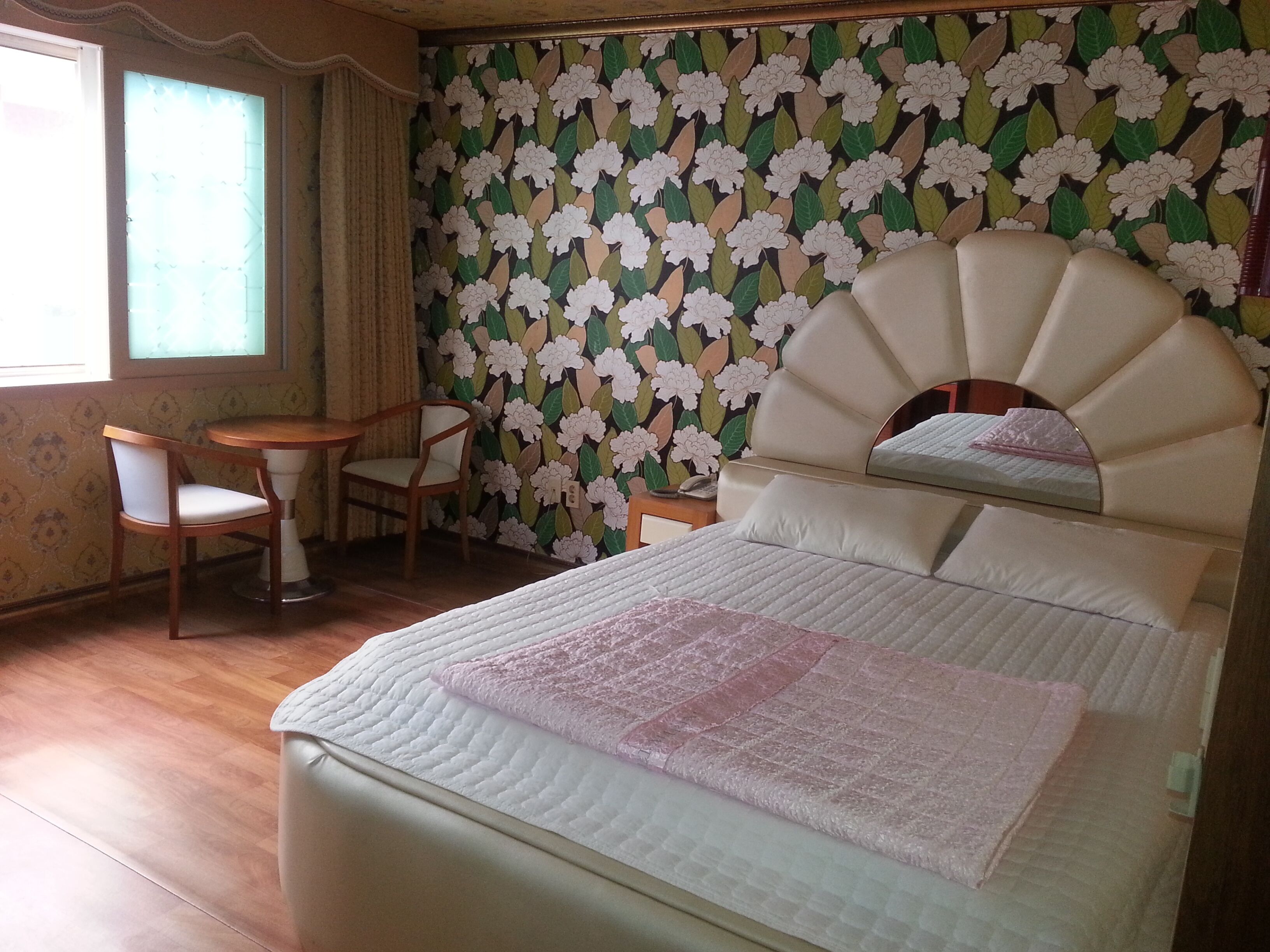 A room with a bed, a chair, a small table, and a window with curtains.