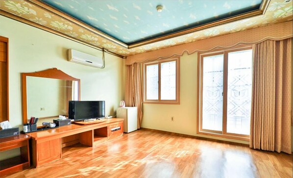 Una habitación con un escritorio de madera, televisión y un amplio ventanal con cortinas.