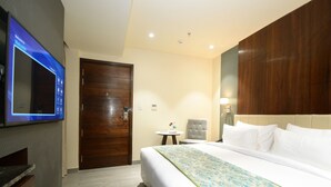 A hotel room with a large bed, a television mounted on the wall, a wooden door, and a small table with a chair. - Everland Wish - A Luxury Boutique Hotel (Jaipur)