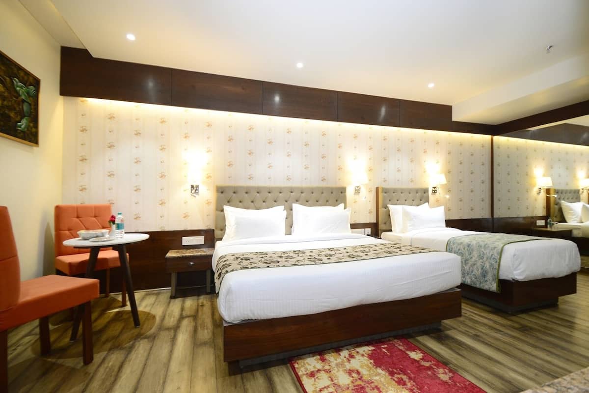 Ein Hotelzimmer mit einem großen Bett, einem kleineren Bett, einer Sitzecke mit einem Sessel und einem Schreibtisch mit Lampe.