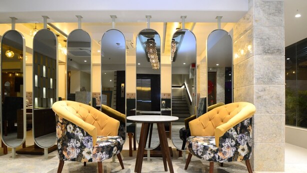 A lobby with a marble floor, two yellow upholstered chairs with floral upholstery, a round table, and a large mirror with a decorative light fixture above it. - Everland Wish - A Luxury Boutique Hotel (Jaipur)