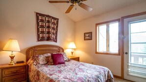 A bedroom with a bed, two bedside lamps, a ceiling fan, a quilt, a window with blinds, and a door. - Deerfield Village 134 - Community Pool, Fire Pit & (Davis)