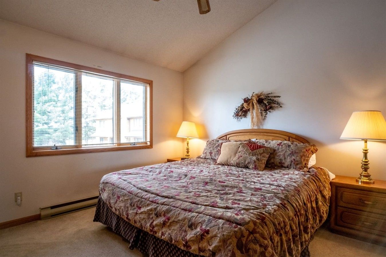 A bedroom with a large bed, two bedside lamps, a window with blinds, and a decorative wall piece.