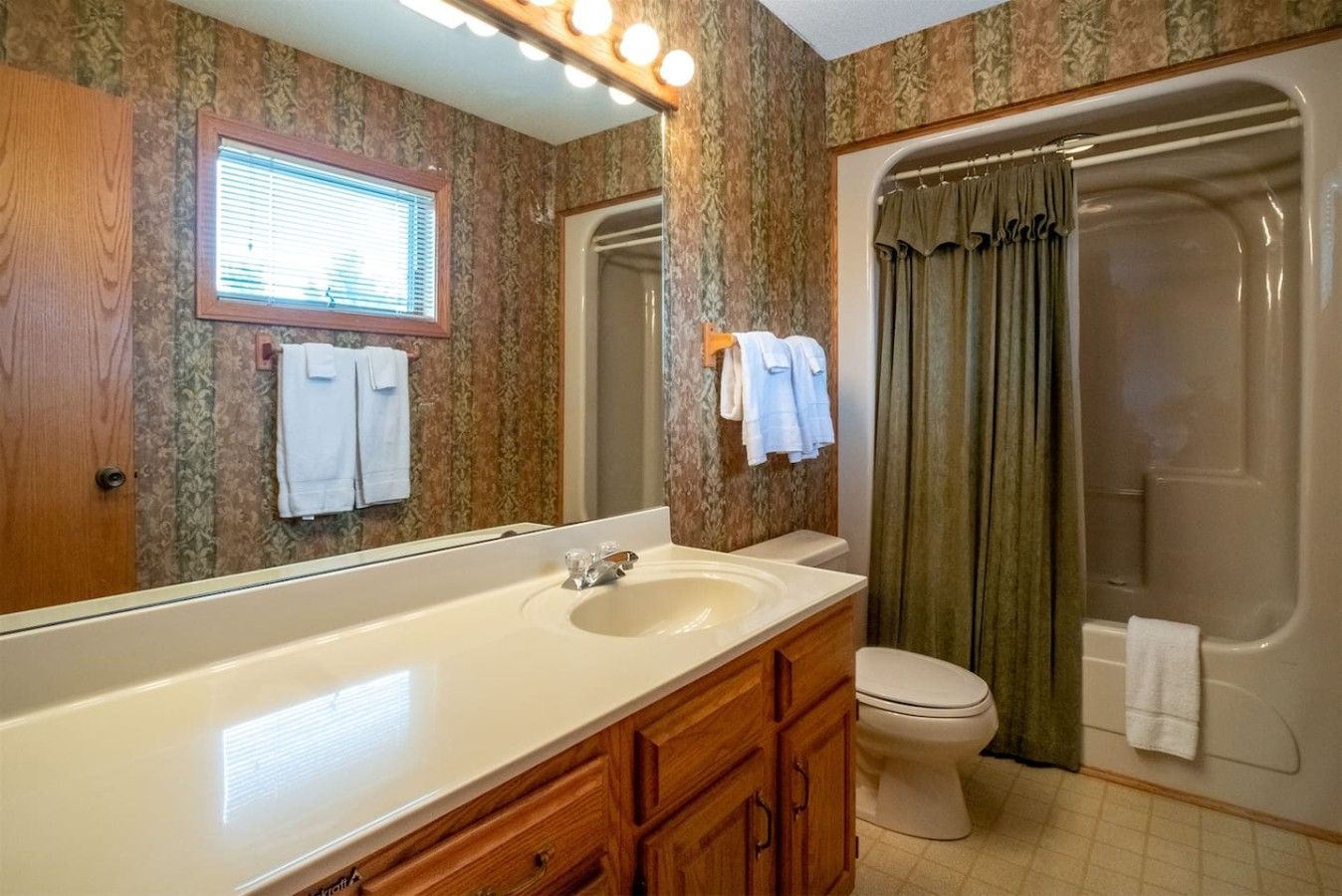 A bathroom with a large mirror, a sink, a toilet, and a shower.