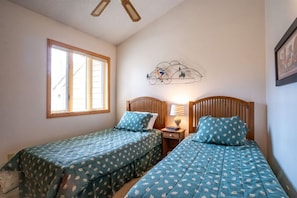 Ein Schlafzimmer mit zwei Einzelbetten, einem Fenster mit Jalousien, einer Wandlampe und einem Deckenventilator.