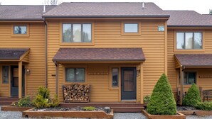 A row of yellow buildings with numbered windows, a firewood stack, and small landscaped gardens. - Deerfield Village 134 - Community Pool, Fire Pit & (Davis)