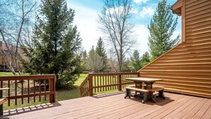 A wooden deck with a picnic table and benches, surrounded by trees and a building. - Deerfield Village 134 - Community Pool, Fire Pit & (Davis)