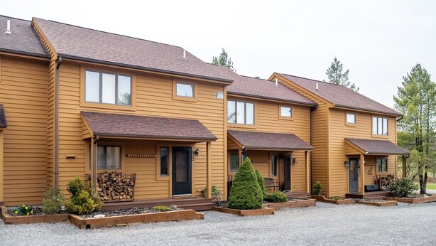 A row of yellow wooden townhouses with front porches, small front yards, and a gravel driveway. - Deerfield Village 134 - Community Pool, Fire Pit & (Davis)