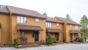 A row of yellow wooden townhouses with front porches, small front yards, and a gravel driveway.