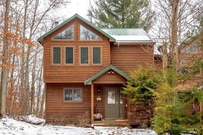 Una baita di legno a due piani con tetto verde, un portico e il numero '10' ben visibile sulla porta.