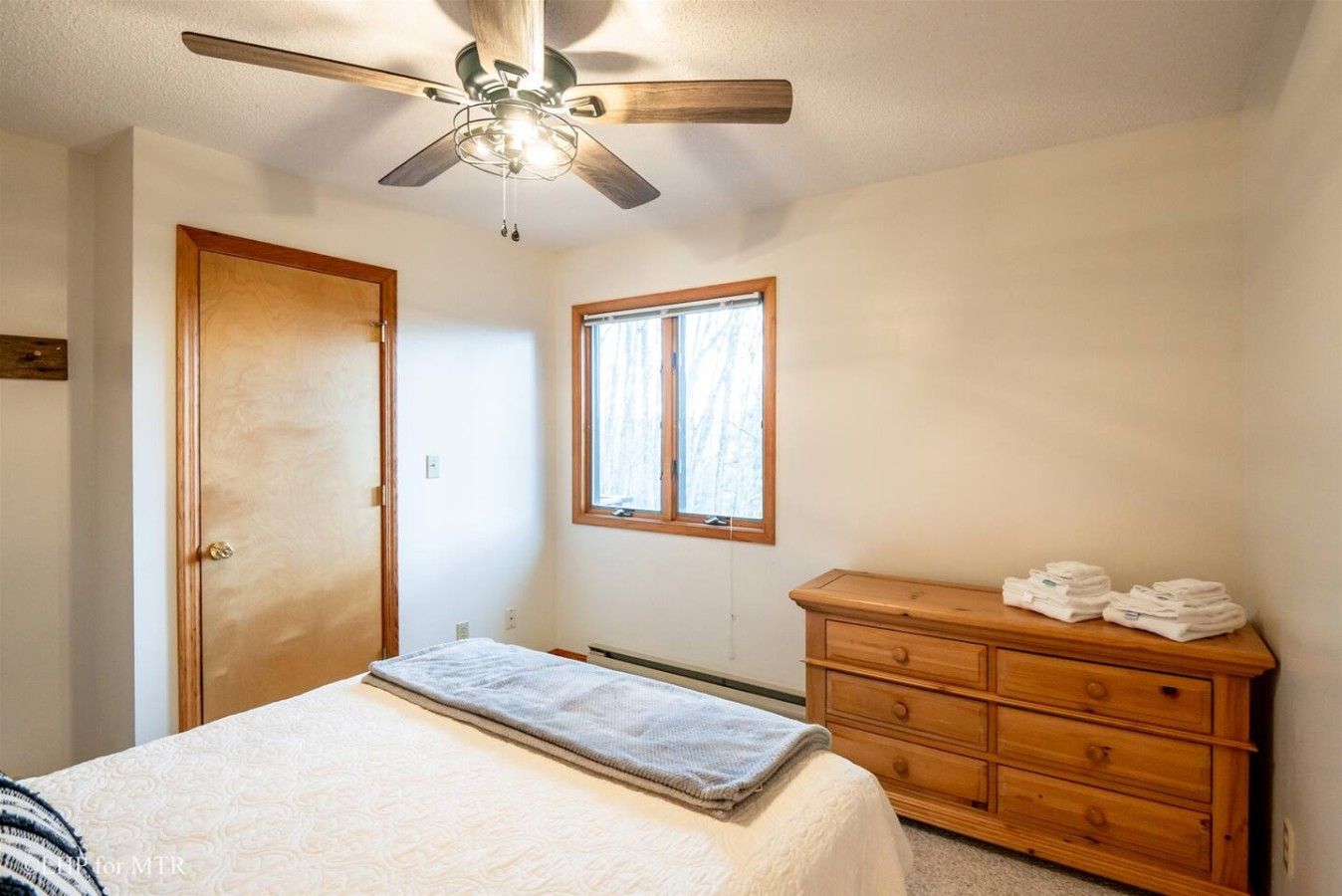 A bedroom with a bed, a wooden dresser, a window, and a ceiling fan.
