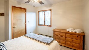 Un dormitorio con una cama, un tocador de madera, una ventana y un ventilador de techo.