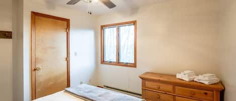 A bedroom with a bed, a wooden dresser, a window, and a ceiling fan.