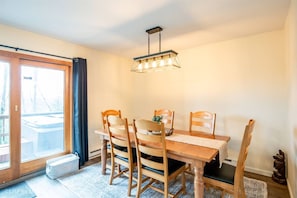 En matplats med ett träbord, fyra stolar, en hängande lampa och utsikt genom en glasdörr.