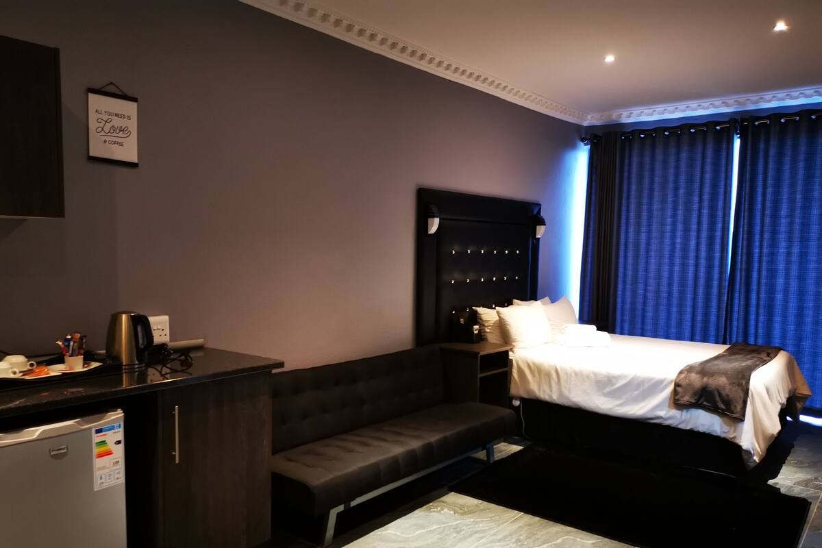 Habitación de hotel con cama, sofá, escritorio con hervidor y un cartel en la pared.