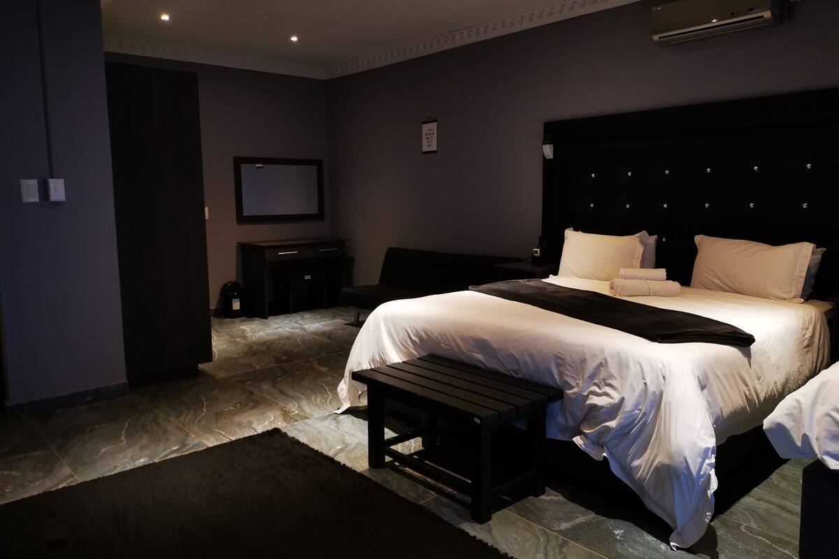 Un dormitorio moderno con una cama grande, un banco y un televisor en la pared.