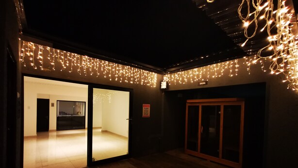 An indoor space with a wooden floor, a glass door leading to a room, and string lights on the ceiling. - Green Olive Panorama (Bethlehem)