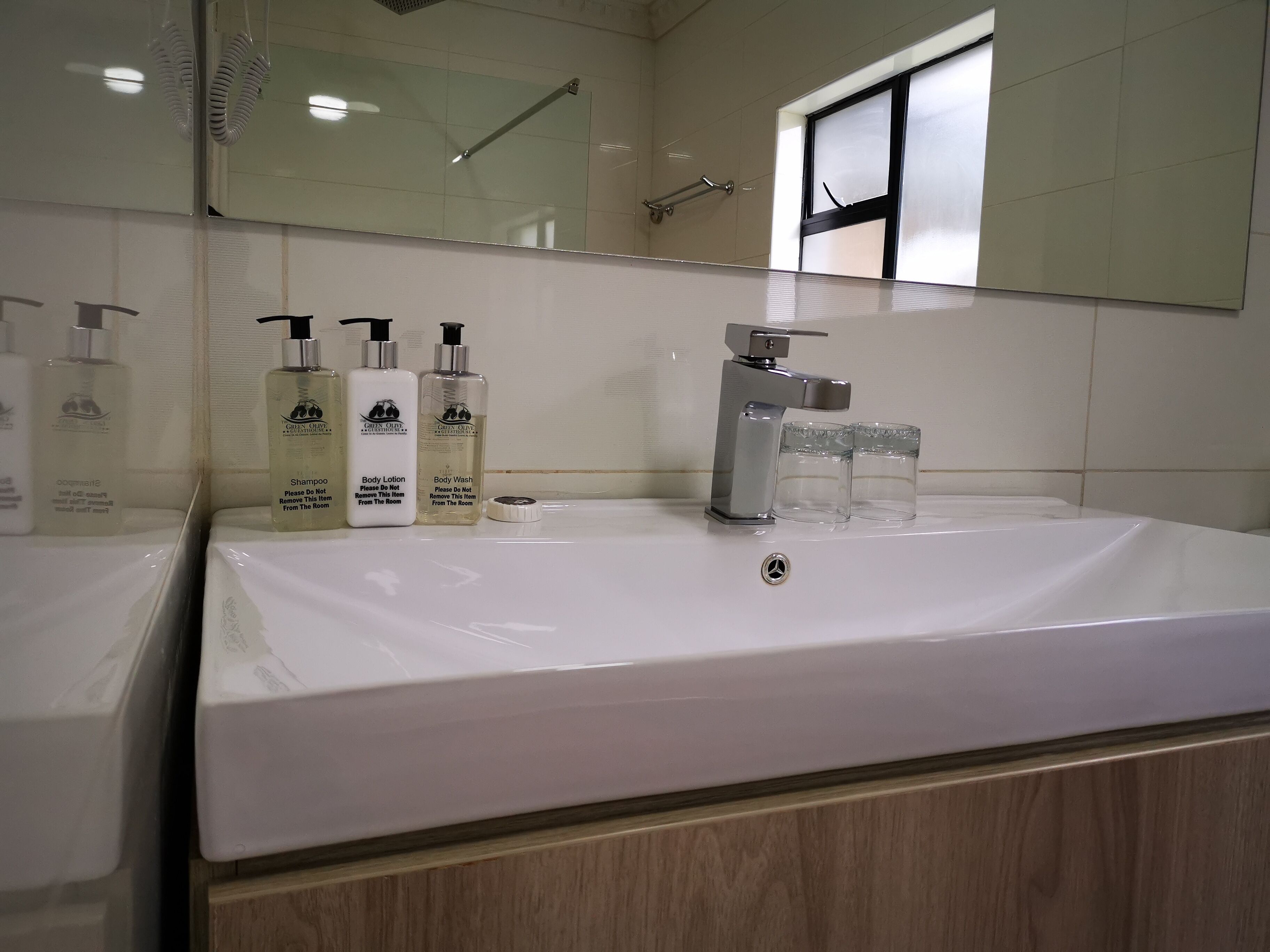 A bathroom with a white sink, three bottles of toiletries, a faucet, and a mirror.