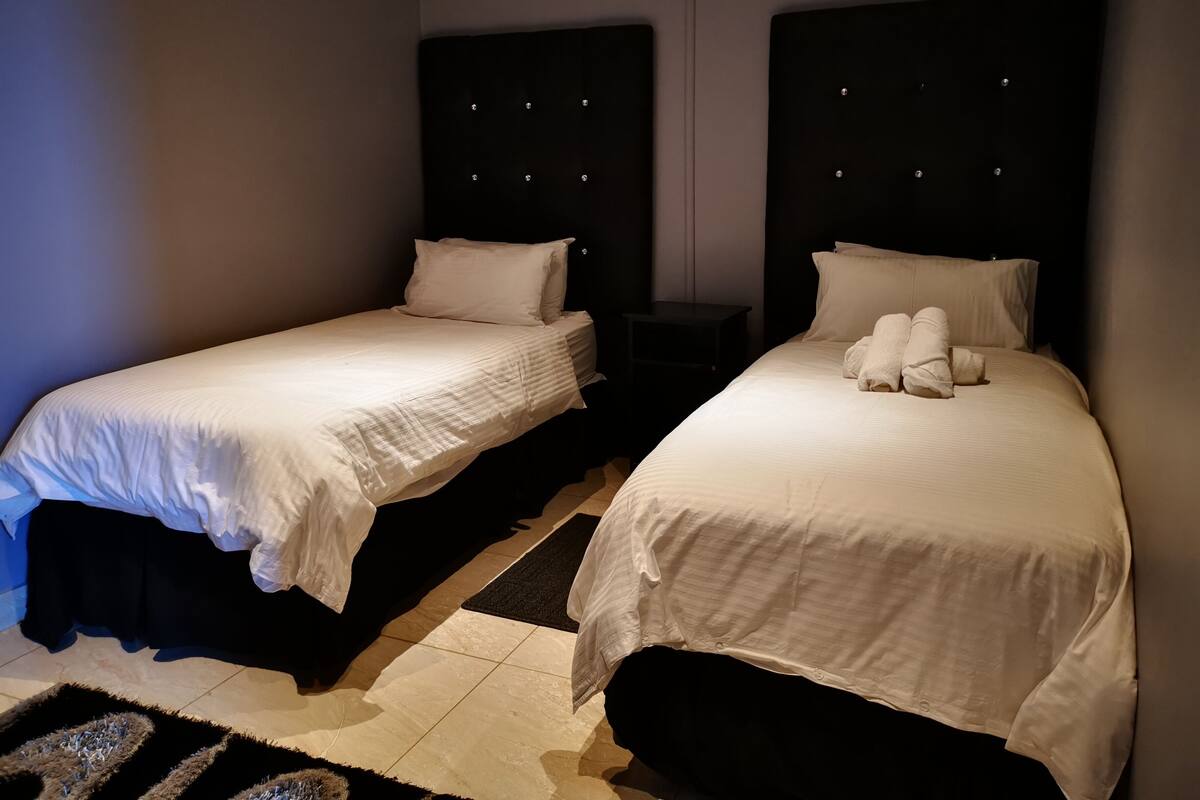 Dos camas individuales con cabeceras, una mesita de noche oscura y una alfombra estampada.