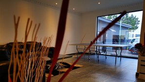 A modern living room with a sofa, a coffee table, and a dining table. There is a large window providing a view of the outside. - Green Olive Panorama (Bethlehem)