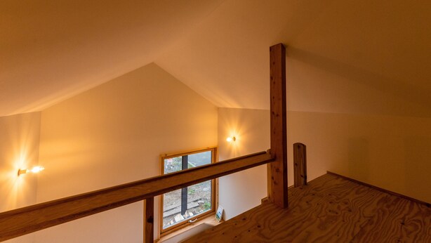 Una escalera de madera con barandilla, un ventanal con vistas al exterior e iluminación en la pared.