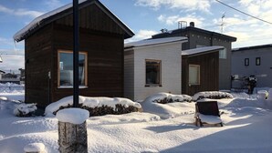 Une cabane en bois avec une petite dépendance attenante, entourée d’un paysage enneigé et sous un ciel dégagé.