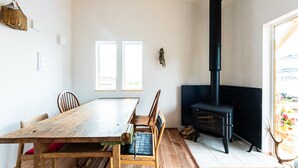 Une pièce avec une table et des chaises en bois, un poêle en bois noir et une fenêtre donnant sur un beau paysage.