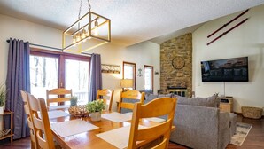 A cozy living room with a stone fireplace, a wooden dining table with chairs, and a grey sofa. - Unwind at Quiet Snow - Mountain Retreat w/ Hot Tub (Davis)