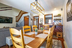 A dining area with a wooden table and chairs, a hanging light fixture, and a staircase leading to another room. - Unwind at Quiet Snow - Mountain Retreat w/ Hot Tub (Davis)