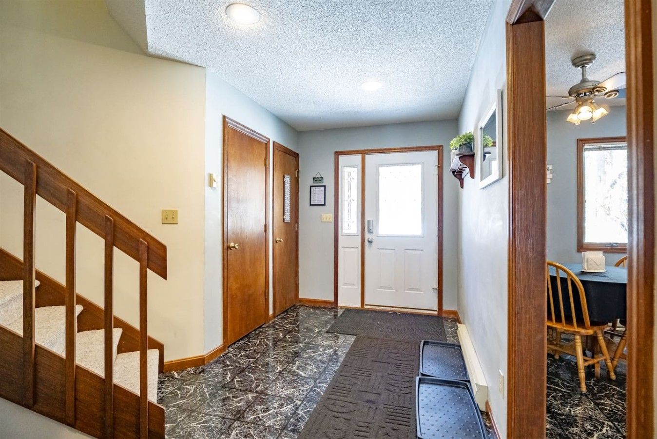 A hallway with a wooden staircase, a door, a ceiling fan, and a window.