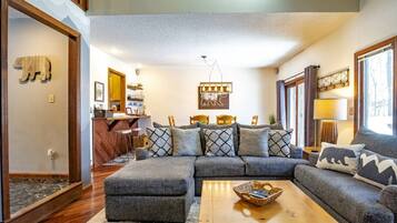 A cozy living room with a sectional sofa, a coffee table, and a kitchen area in the background.