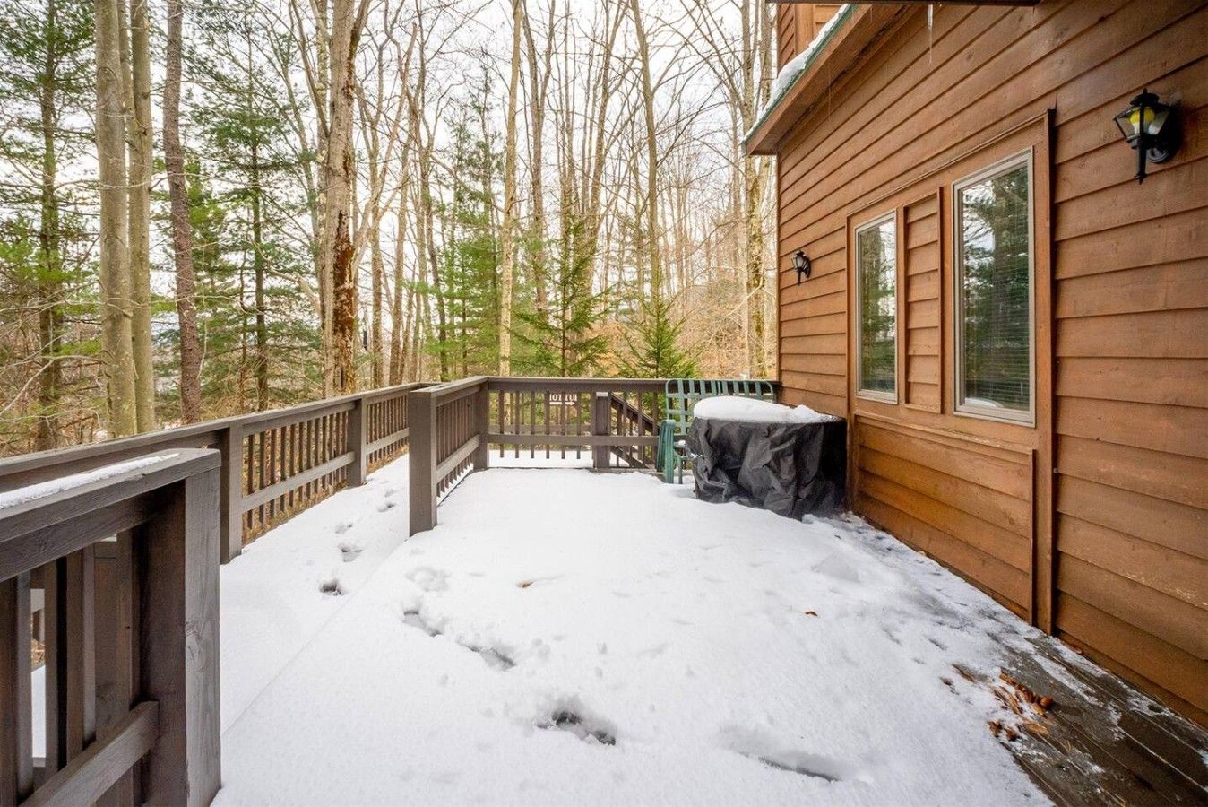 A wooden deck with snow, a covered table, and a railing.