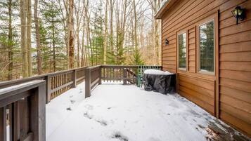 A wooden deck with snow, a covered table, and a railing.