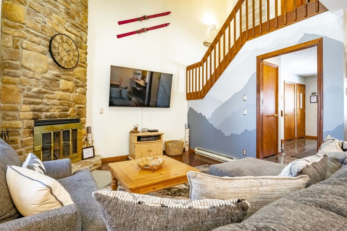 Un salon avec un mur en pierre, une cheminée, un téléviseur à écran plat, un escalier en bois et une fresque représentant une montagne.